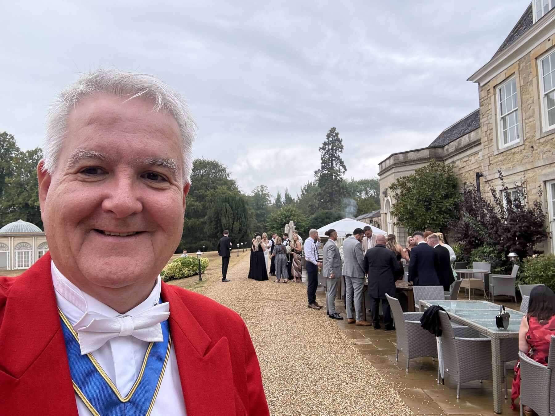 Andrew Morgan as toastmaster among wedding guests on the terrace of a country house venue